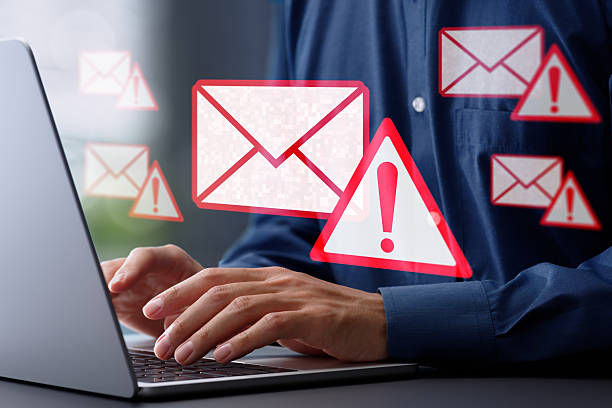 istock Spoofed emails and phishing scams with malicious attachments. Email and warning icons with exclamation marks. Man using laptop computer to check and respond to emails. 2208603072