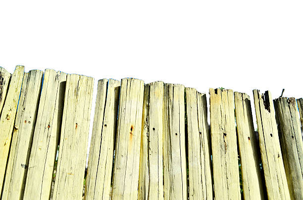 A row of weathered wooden planks forms a rustic fence, displaying irregular tops, visible knots, and discoloration. Its rough texture and aged charm make it ideal for themes of countryside aesthetics.