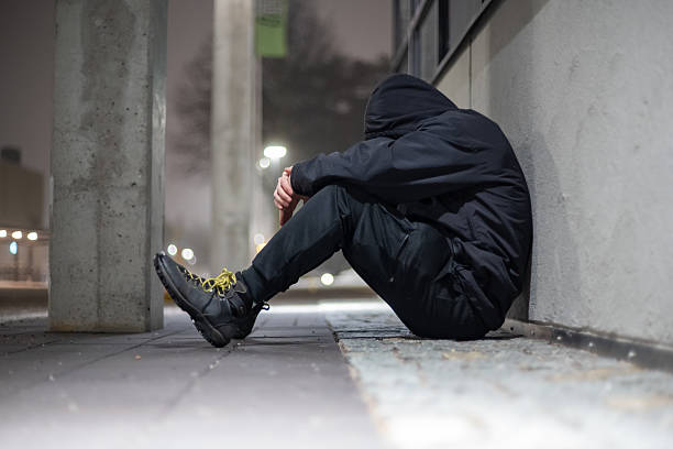 istock depressed hooded man sitting on a street during night time. 2208609955