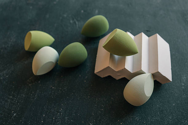 istock Soft green makeup sponges on dark textured surface with one resting on a geometric pedestal. Minimalist flat lay of beauty blenders in various shades of green 2208617118