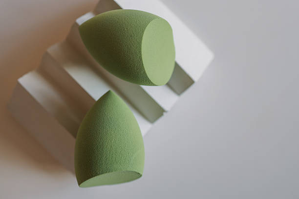 istock Soft green makeup sponges on light textured surface with one resting on a geometric pedestal. Minimalist flat lay of beauty blenders in various shades of green 2208617123