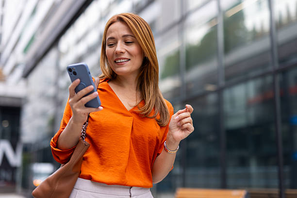 istock Smiling businesswoman using smartphone while walking in city 2208621040