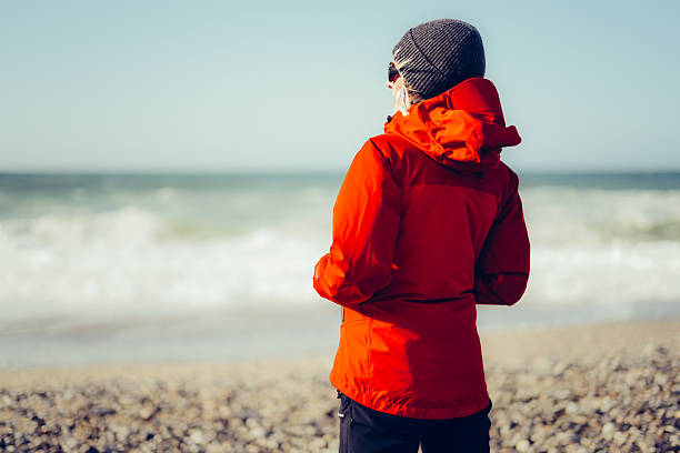 Rear view of a woman in winter, standing alone on the stoney beach at Portreath on the north Cornwall coast of England, UK.