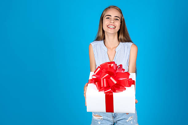 istock Young girl holding gift box on blue background 2208624576