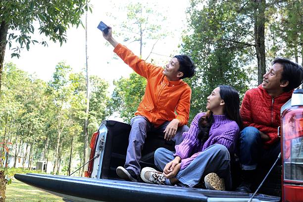 istock Three Young People Taking Selfie using Mobile Phones While Sitting at the Car Trunk 2208625593
