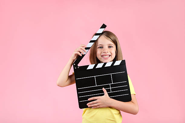 istock Little girl with clapper board on pink background 2208626574