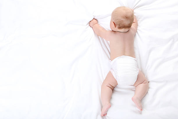 Adorable baby in white sunny bedroom. Newborn child relaxing in bed. Nursery for young children. Textile and bedding for kids. Family morning at home. New born kid during tummy time with toy bear.