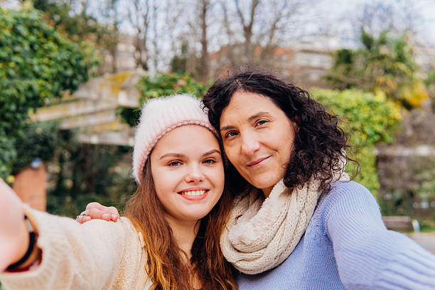 istock Mother and daughter taking selfie together, laughing warmly while wearing winter jackets, surrounded by park greenery under soft daylight 2208632941