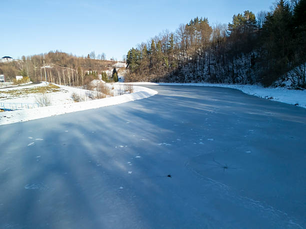 A tranquil winter scene featuring a frozen river winding through a snowy landscape, surrounded by trees and clear blue sky. Ideal for seasonal themes.