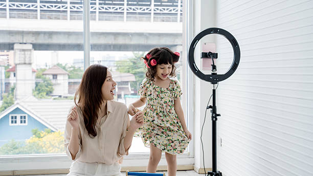 istock Happy mom and daughter dancing while recording video at home using smartphone and ring light, creating fun family content and enjoying quality bonding time. 2208634809