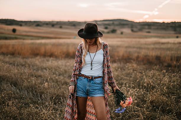 Beautiful blonde woman stands in a field, holding a vibrant flower bouquet and embracing the peacefulness of nature.
