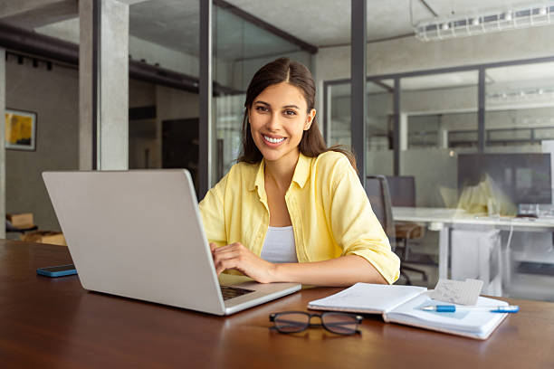 istock Portrait at camera smiling latin female studying student, professional it specialist working at laptop computer sitting at desk in modern office. Cheerful young woman employee using pc for business 2208637362