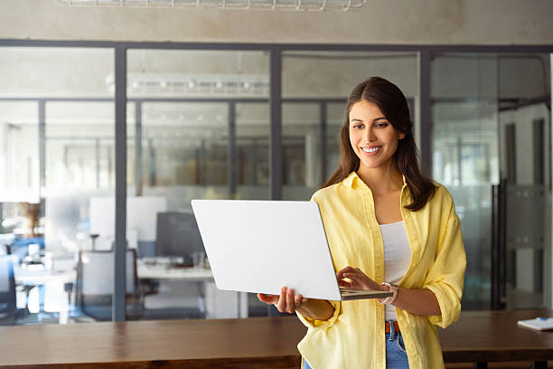 istock Smiling latin hispanic female marketing manager, professional it specialist working, browsing at laptop computer standing at workplace in office. Young woman employee using pc for business. Copy space 2208637392