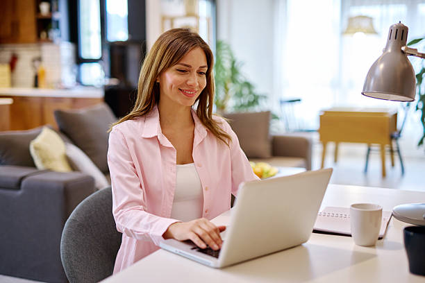 istock Young woman working from home using laptop, smiling and looking at screen 2208639351