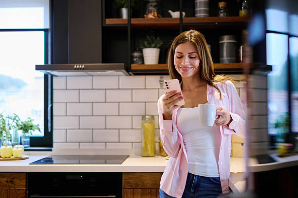 istock Woman enjoying morning coffee and using smartphone in modern kitchen 2208639406
