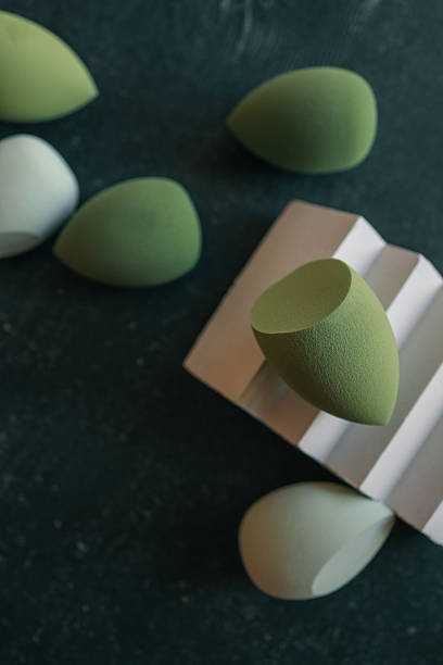 istock Soft green makeup sponges on dark textured surface with one resting on a geometric pedestal. Minimalist flat lay of beauty blenders in various shades of green 2208647101