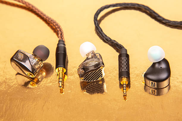 istock Three earbuds with woven cables and gold-plated jacks on a reflective golden surface, ideal for tech product shots and audio accessory themes. 2208649925