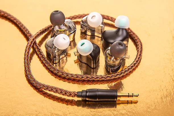 istock Three pairs of wired earbuds with braided cables and 3.5mm plugs on a reflective gold surface, ideal for tech and audio gear themes. 2208650076