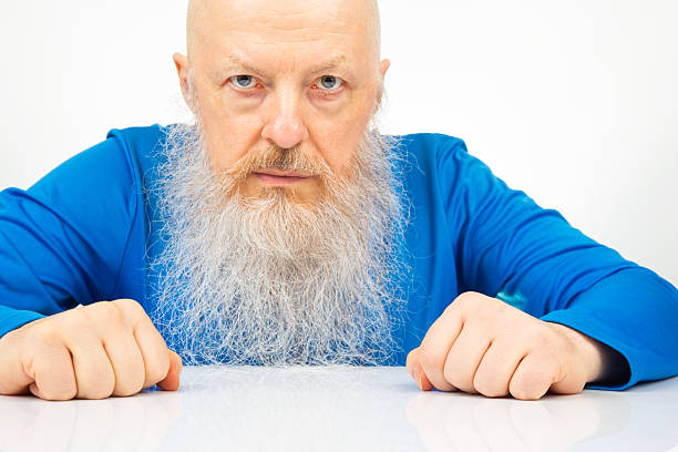 portrait of a serious man with a large gray beard on a light background.