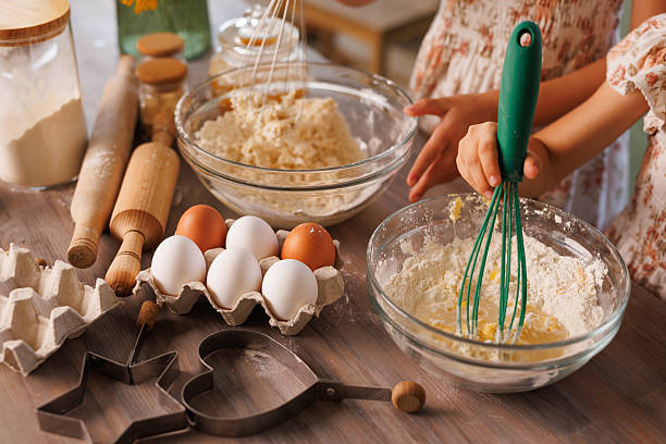 istock Kids baking cookies, mixing flour and eggs with kitchen utensils on a wooden table. 2208653966