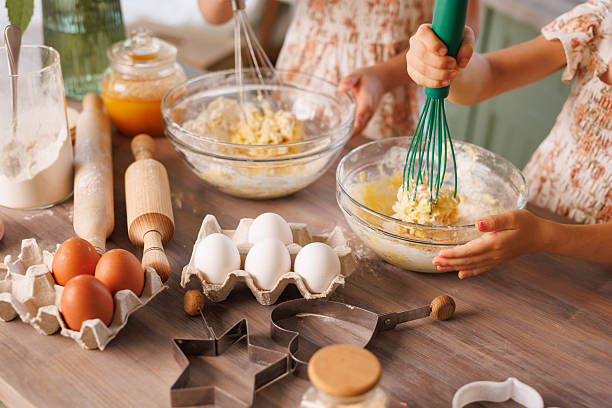 Kids mixing dough with whisks among eggs, tools, and flour on a rustic kitchen table.