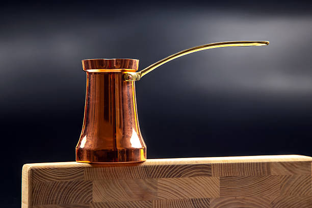 istock A shiny copper Turkish coffee pot with a brass handle balances on a wooden edge against a dark gradient background, ideal for coffee culture and kitchen themes 2208655153