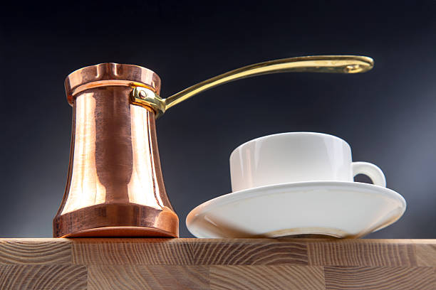 istock A shiny copper Turkish coffee pot with a brass handle beside a white ceramic cup and saucer, balanced on a wooden cutting board against a dark background, perfect for coffee culture photography 2208657206