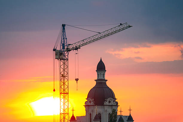 Construction of a Christian church building using a construction crane against a sunset background