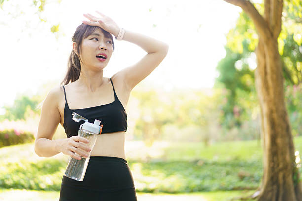 istock Asian woman take a break and drinks water from bottle after finished running. 2208667124