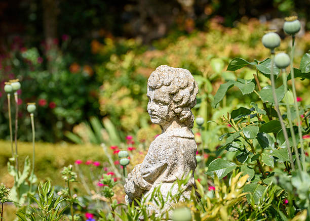 Statue of a boy placed among colourful flowers in a garden setting, captured in natural outdoor light.