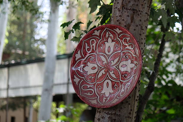 Decorative ceramic plate displayed on a tree in a vibrant garden setting during daylight hours