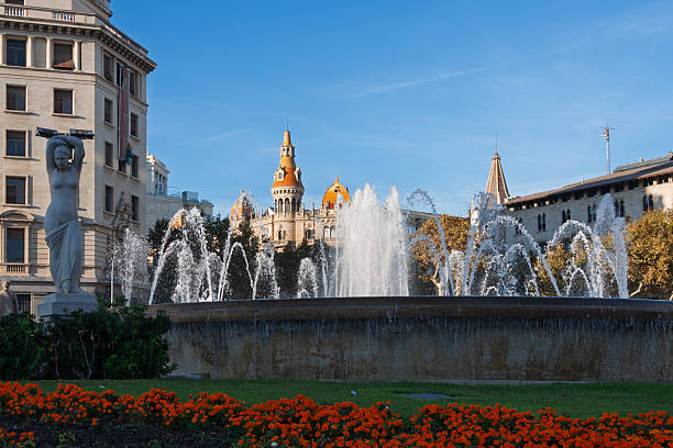 Barcelona, Spain. November 13th, 2010:\nA beautiful fountain with cascading water surrounded by vibrant orange flowers, set against the stunning architecture of Barcelona's historical buildings. The warm glow of the setting sun adds a magical touch to the scene, highlighting the classical design and creating a serene atmosphere. In the background, the architecture stands tall, with intricate details and the iconic rooftop structures of the city.