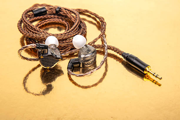 istock Three earbuds with woven cables and gold-plated jacks on a reflective golden surface, ideal for tech product shots and audio accessory themes. 2208677438