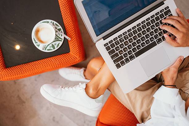 Overhead view of a person using a laptop while seated on a comfortable chair. A cappuccino sits on a table nearby, creating a cozy and productive work environment