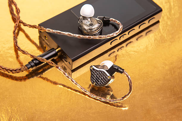 istock Wired earbuds with a woven cable on a sleek black audio player, set on a reflective gold surface. Ideal for technology, sound, and modern design concepts 2208679650