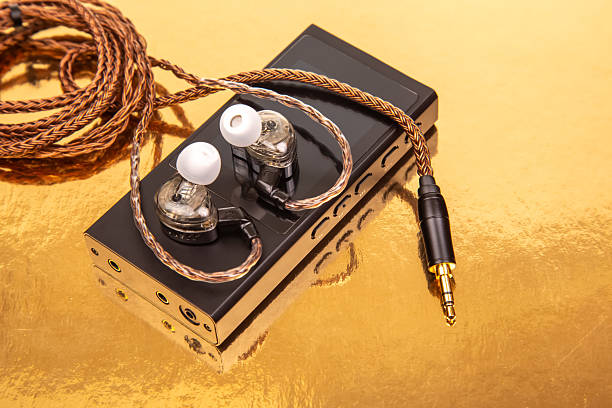 istock Wired earbuds with a woven cable on a sleek black audio player, set on a reflective gold surface. Ideal for technology, sound, and modern design concepts 2208679720