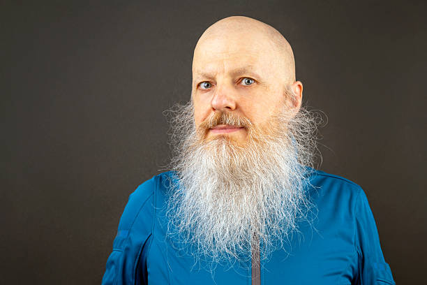 Elderly man with a long, white beard smiling widely against a dark background. His bright eyes and bald head emphasize his cheerful and friendly demeanor