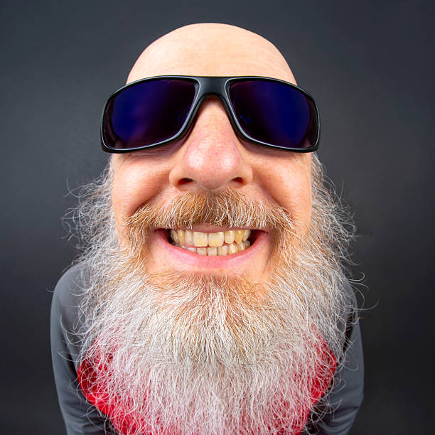 Elderly man with a long, white beard smiling widely against a dark background. His bright eyes and bald head emphasize his cheerful and friendly demeanor