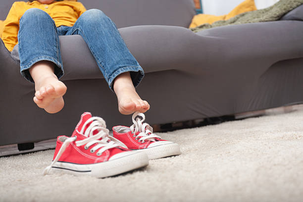 istock Barefoot child on sofa with sneakers on the floor – copy space 2208684406