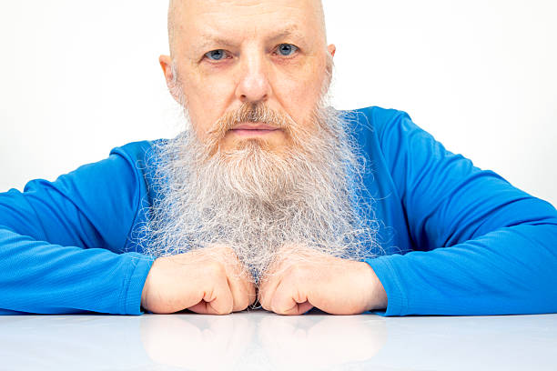 portrait of a serious man with a large gray beard on a light background.
