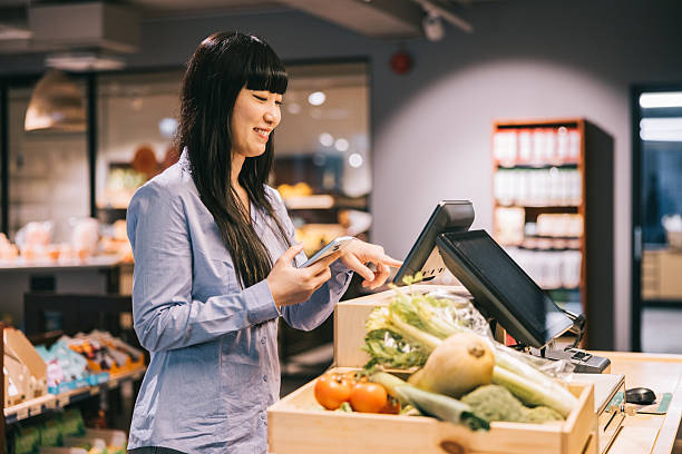 istock Holding a smartphone, a female customer effortlessly uses the self-service terminal to complete her transaction at the organic store 2208690984