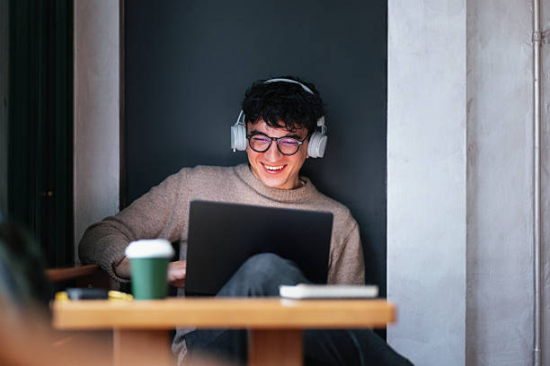 istock Smiling Enthusiast Using Laptop and Headphones in Relaxed Cafe Environment 2208695148