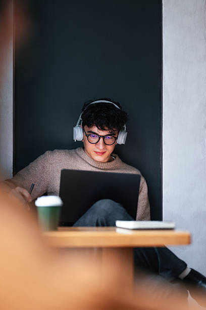 Focused Student Wearing Headphones Using Laptop in Cozy Cafe Study Setup