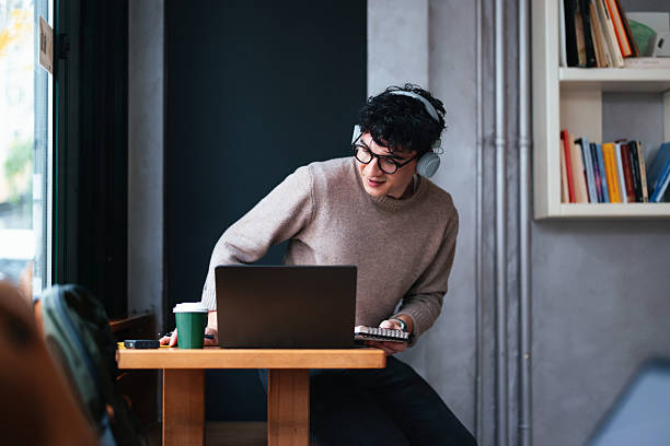 istock Young Man Using Laptop and Headphones in a Cozy Cafe Setting 2208695687