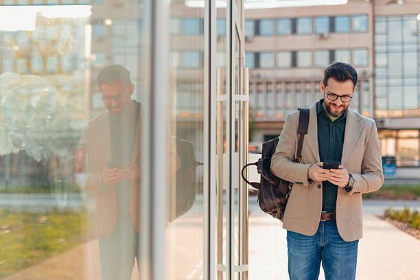 istock Businessman using smartphone while walking near modern glass building 2208700100