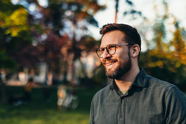 istock Smiling young man with eyeglasses looking away in a park during sunset 2208700217
