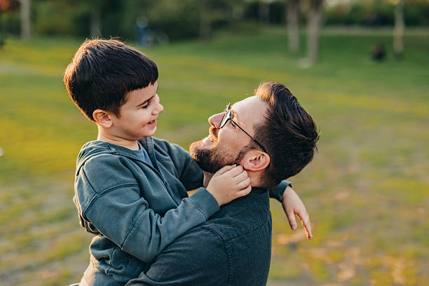 istock Father holding and looking at his son in a park during sunset 2208700549