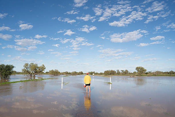 Man walking in the flooded road toward King Creek crossing in between Cluny Station and Bedourie,QLD.