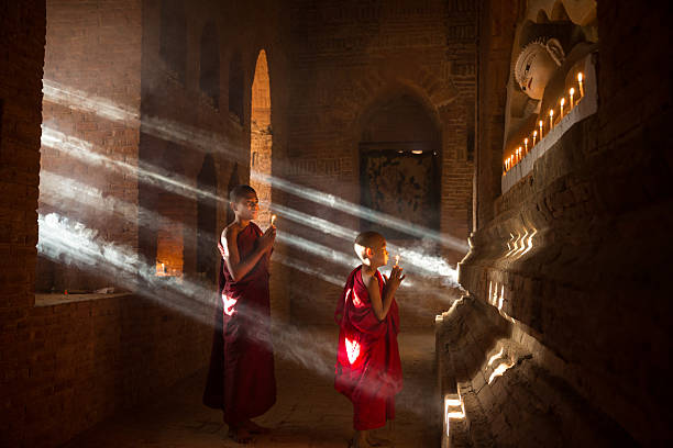 istock Two young Buddhist monks pray in a mystical atmosphere inside an ancient temple 2208764275