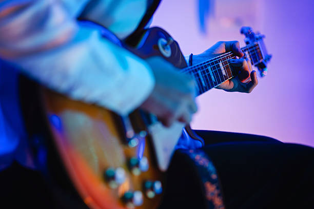 The volume and tone knobs are in focus on an electric guitar hanging on a wall. The perspective shows a crop of a front guitar with part of another electric guitar in the background.